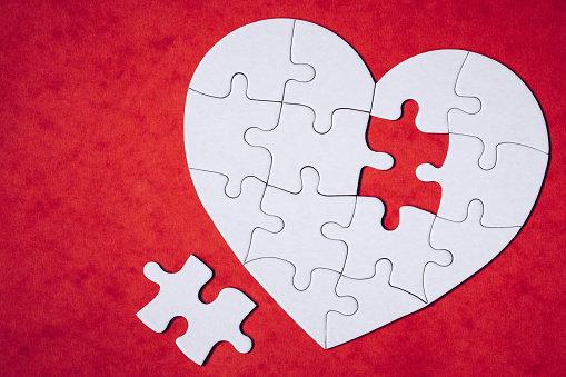 Heart-shaped jigsaw puzzle on color background. Puzzle heart on wooden background. A missing piece of the heart puzzle. Heart shape jigsaw puzzle. Puzzles in the shape of a heart.