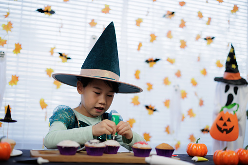 young Asian girl with witch costume decorating cupcake for haloween party