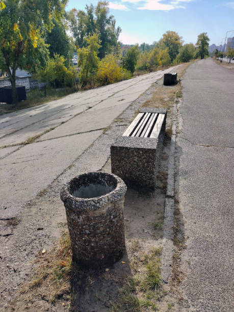 istock Stone decorative trash can and park bench in perspective against blue sky and trees 1819180249