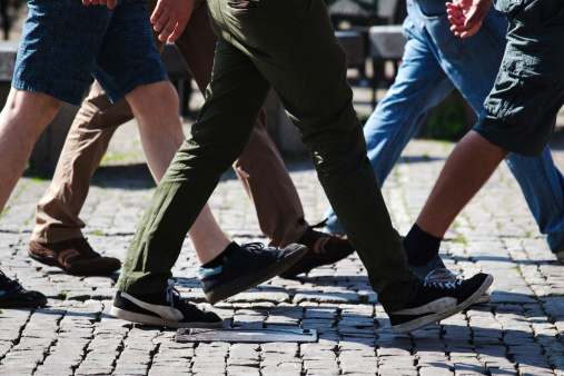 legs of men walking on a cobblestone square in the city
