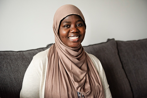 Muslim black woman portrait at home in living-room. She is from African descent living in North America. This is part of a series. Horizontal waist up indoors with copy space. This was taken in Montreal, Quebec, Canada.