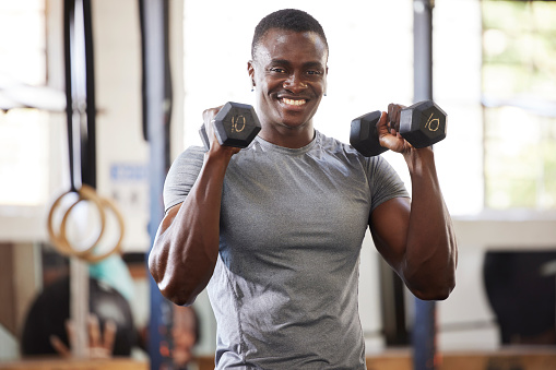 Fitness, weights and portrait of a black man lifting for muscle, training and power in the gym. Smile, strong and African athlete doing a workout, exercise or sports for body building and cardio