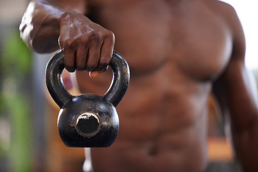Kettlebell in hand, black man and fitness in gym, bodybuilder with muscle training and weightlifting exercise. Fist, strong person and bodybuilding for power and strength, health and active lifestyle
