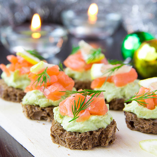 Appetizer canapes of bread with avocado, red fish salmon, lemon Delicious appetizer canapes of black bread, avocado and red fish salmon on board for New Year's celebratory table restaurant food canapes appetizers stock pictures, royalty-free photos & images