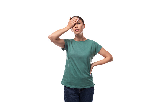 young forgetful brunette woman dressed in a green t-shirt on a white background.