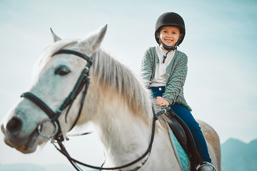 Ranch, happy and girl child on a horse to practice riding for a championship, competition or race. Happiness, animal and kid with smile practicing to ride a pony pet on a field or farm in countryside