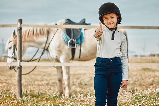 Happy, thumbs up and horse with portrait of girl in countryside for approval, equestrian and adventure. Winner, goals and smile with child jockey on animal ranch for pet care, pasture and leisure