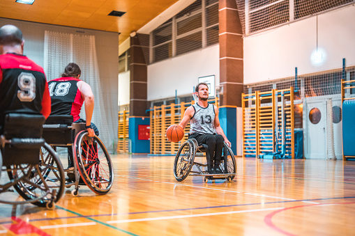 Rear view of male wheelchair basketball players rolling into position during practice game.  Rotating and passing the ball.