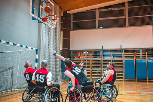 Aggressive male wheelchair basketball players struggling for control of ball during practice game.