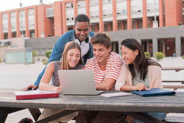 istock Group multi-ethnic smiling teenage students using laptop while looking information for an academic project outdoors. Meeting of diverse university young people enjoying while watching educational video on computer. 1819346206