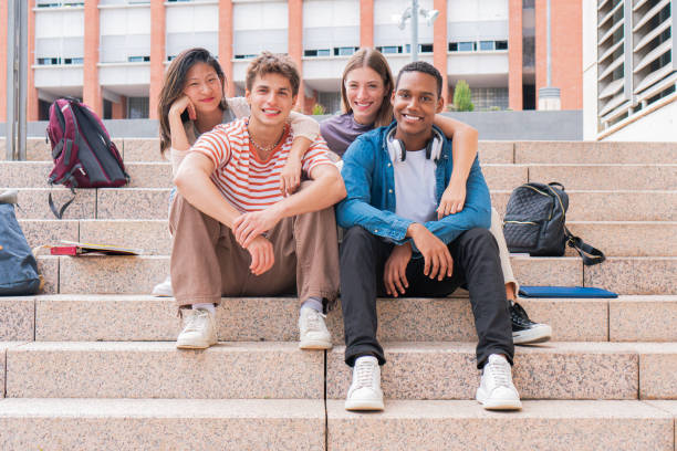 istock A group of multiracial students sitting on steps with backpacks and folders and books, looking at camera and smiling. Portrait of multiethnic teenager friends on college stairs laughing 1819352419