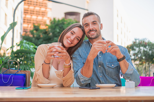 Boyfriend and girlfriend in a date drinking a cup of coffee in a restaurant smiling and looking at camera. Portrait of two young adults male and female together closeness in a daytime enjoying drinks