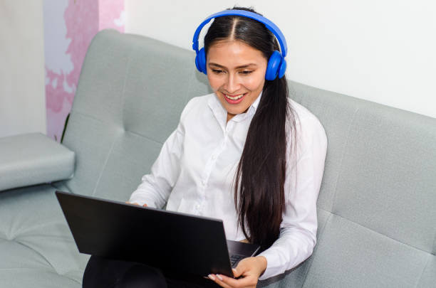 istock Young woman sitting on a couch using her laptop and wireless headphones 1819371280