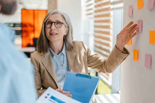 istock Business woman, successful scrum master talking with colleague, explaining something using sticky notes, agile methodology for productivity, working in modern office. Teamwork, scrum concept 1819385710