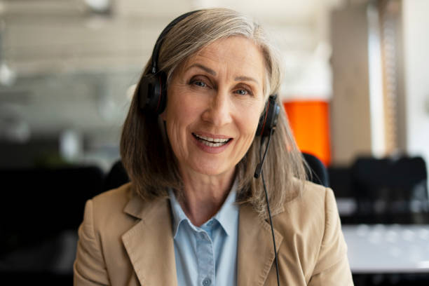 istock Smiling senior woman, call center operator answering call, communication with customer sitting in modern office. Serious freelancer having video call working from home. Successful business 1819385712