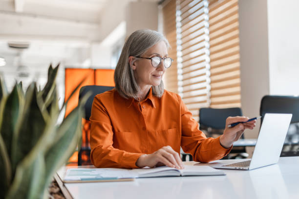 istock Confident senior woman, manager using laptop computer working online sitting in modern office. Business woman wearing stylish eyeglasses checking email. Technology concept 1819385721