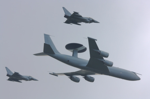 A Boeing E3 Sentry AWACS (Airborne Warning & Control System) or AEW (Airborne Early Warning) aircraft is escorted through a stormy sky by two Eurofighter Typhoons.