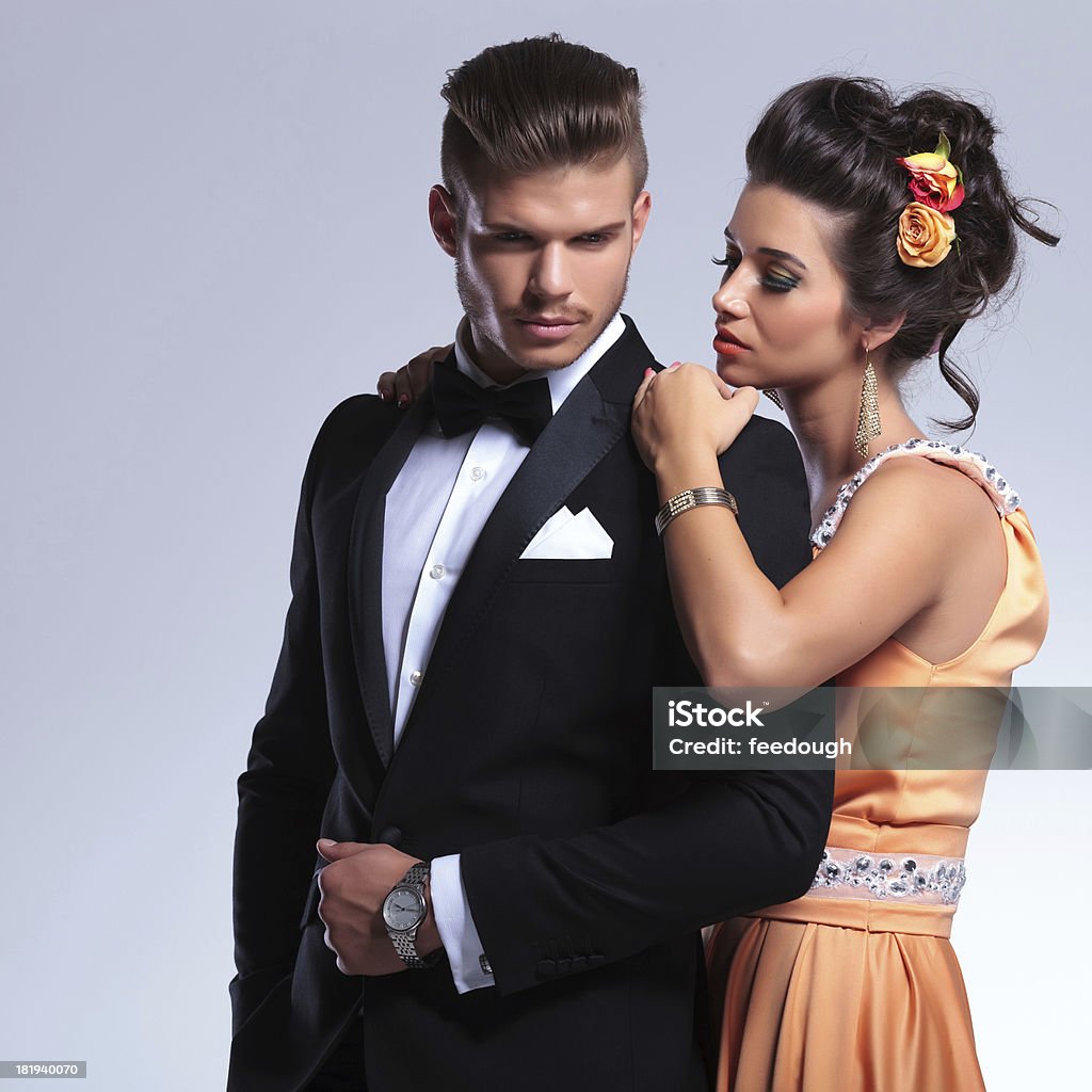 fashion couple where woman is with hands on his shoulders young fashion couple with woman behind man, holding her hands on his shoulders while both looking away from the camera. on gray background Adult Stock Photo