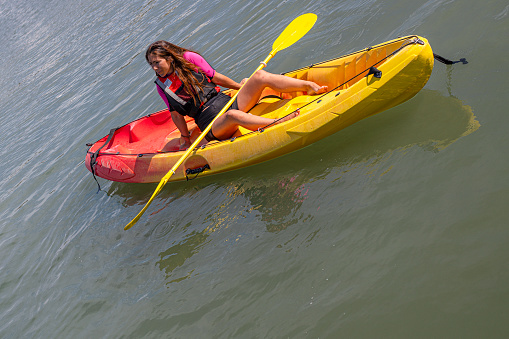 calm and relaxed caucasian young girl looking at the horizon sitting in a kayak relaxed with the paddle on her legs
