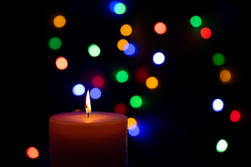 Advent candle with defocused multicolor lights at backround.