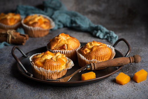 Fresh muffins with pumpkin in a decorative bowl on a rustic gray background