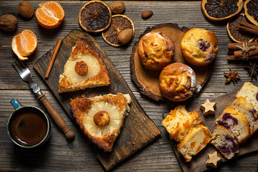 Pieces of sweet pie with pineapple, muffins and cup of coffee on a rustic wooden table