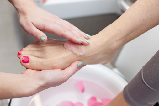 Beautitian in the spa salon applying foot scrub salt.