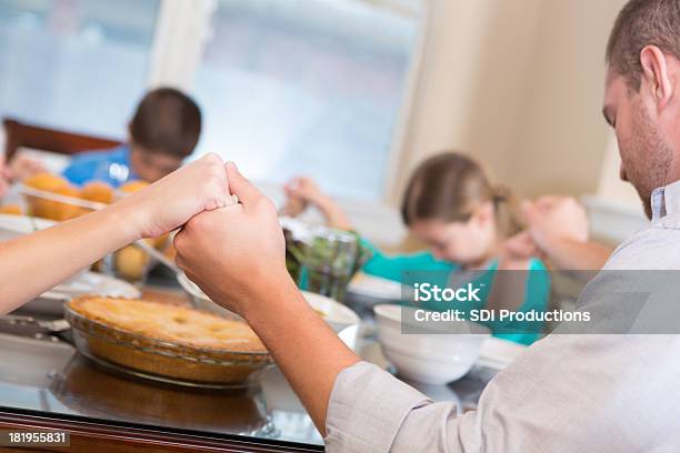 Família Juntar As Mãos A Rezar Durante Refeição Na Mesa De Jantar - Fotografias de stock e mais imagens de De Mãos Dadas