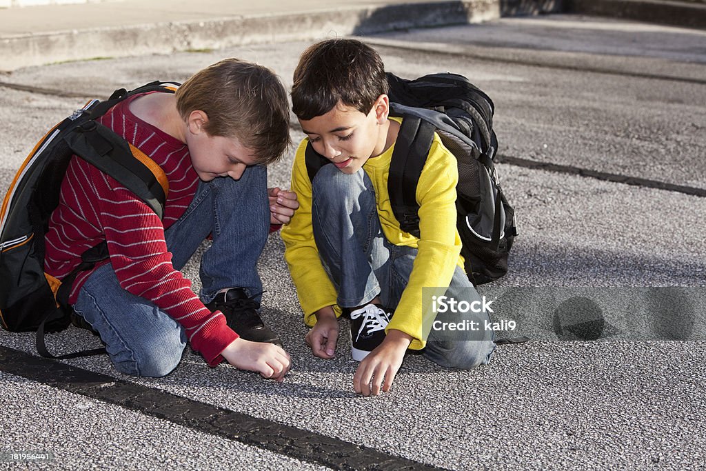 School boys kneeling on the ground, playing Elementary school boys (9 years) with backpacks kneeling on the ground, playing. Boys Stock Photo