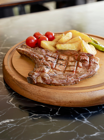 Delicious steak  and fries serving on cutting board on top of a marble restaurant table