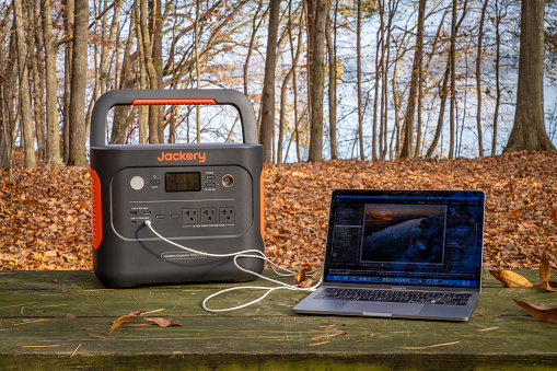 Colbert Ferry Park, AL, USA - November 23, 2023: Jackery Explorer 1000 Plus Portable Power Station is charging MacBook Pro laptop on a picnic table on a shore of Tennessee River.