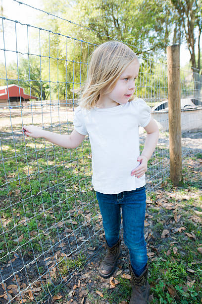 Little Girl On a Farm "This is a vertical color photograph of a little girl on a farm in Plant City, Florida. She holds onto a fence. There is a barn in the background." plant city photos stock pictures, royalty-free photos & images