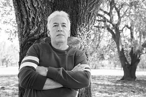 Cuban Man Stands Tall by Florida Tree "This is a horizontal, black and white photograph of a casually dressed, mature Cuban man with white hair standing in front of a tree on a Florida farm. He smiles as he looks into the camera." plant city photos stock pictures, royalty-free photos & images