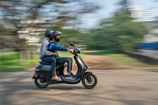 Pune, Maharashtra, India: - December 7th, 2021 : Slow shutter, Motion blur image of a men wearing helmets for safety, riding on a blue electric moped.
