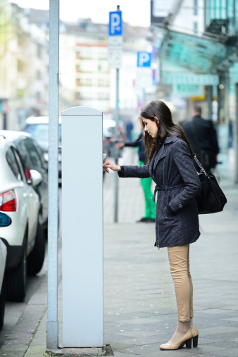 Young adult woman using the parking meter.
