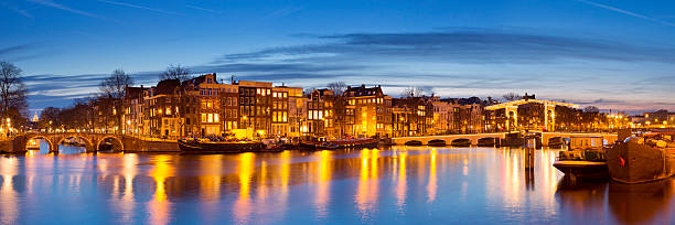 The famous Magere Brug ('Skinny Bridge') on the Amstel River in Amsterdam, The Netherlands at dusk. A seamlessly stitched panoramic image.