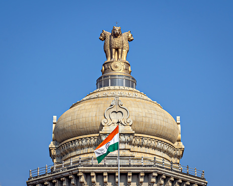 Close up image of dome of largest legislative building in India - Vidhan Soudha , Bangalore with nice blue sky background. Translation of text mentioned is Government work is God's work.