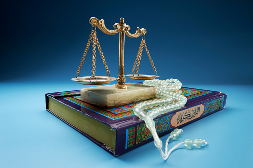 libra scale and  prayer beads on the holy quran against blue background