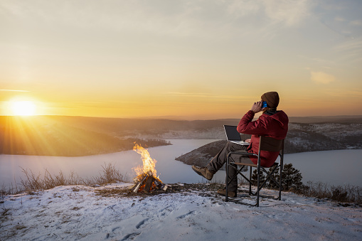 businessman talking on his phone and using a laptop during winter holiday in nature. . freedom, remote work concept.