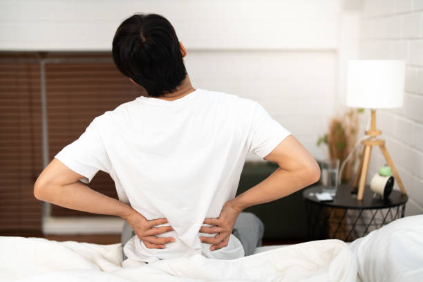 azjatycki bezsenny mężczyzna dotykający bólu pleców o chorobie syndromu biurowego, ponieważ ciężko pracuje na co dzień, siedząc na łóżku przed snem w domu - backache lumbar vertebra human spine posture zdjęcia i obrazy z banku zdjęć