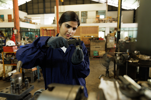 Indian engineer woman using vernier caliper measuring work piece in factory