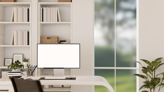 A modern white office workspace with a white-screen computer monitor mockup on a desk, a houseplant, bookshelves, and accessories. 3d render, 3d illustration