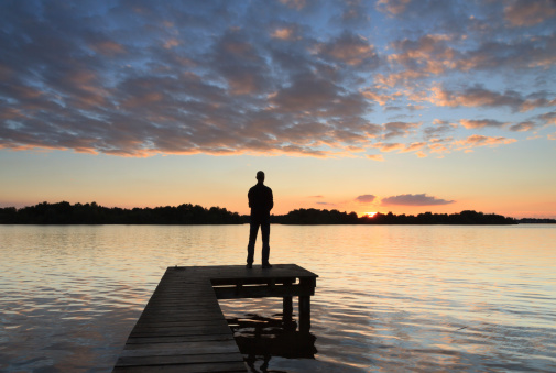 Man on a jetty enjoying the colorful sunset over a lake.