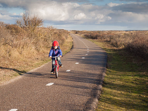 small boy in cycle helmet cycling towards camera along a cycle path through the dune landscape of the dutch north sea coast