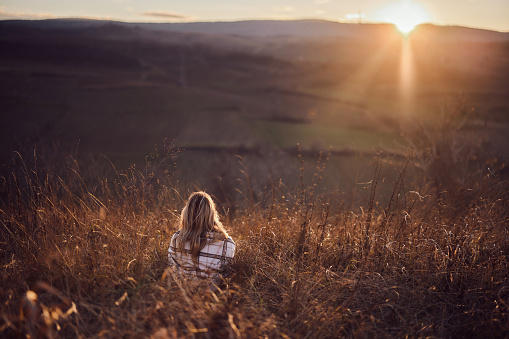 Back view of a woman looking at sunset view while relaxing in tall grass. Copy space.