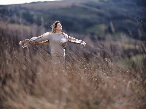 Carefree woman having fun with her arms outstretched during autumn day in tall grass on a hill. Photographed in medium format. Copy space.