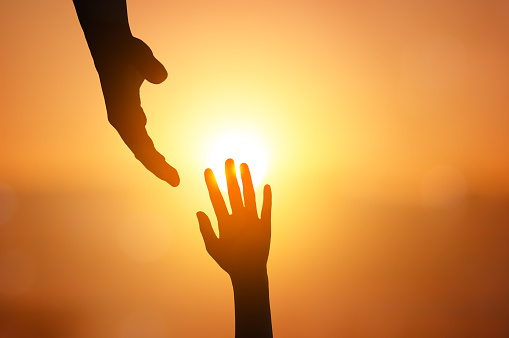Silhouette of hand helping on sunset background