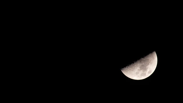 Half moon in the dark night moving down and disappearing from the horizon.