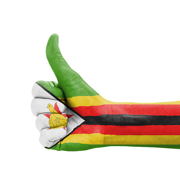 Harare, Zimbabwe: low-angle photograph of the National Flag of the Republic of Zimbabwe waving in the wind against blue sky. The flag features seven even horizontal stripes of green, gold, red, and black, with a white triangle at the hoist. The green stripes represent the country's agriculture and vegetation; the gold symbolizes mineral wealth; the red denotes the blood shed fighting in the Rhodesia civil war; and the black represents the heritage of the native African majority. The white triangle signifies peace and contains a red five-pointed star representing the nation’s aspirations, overlaid with the Golden Zimbabwe Bird, the national emblem derived from the historic Great Zimbabwe ruins.