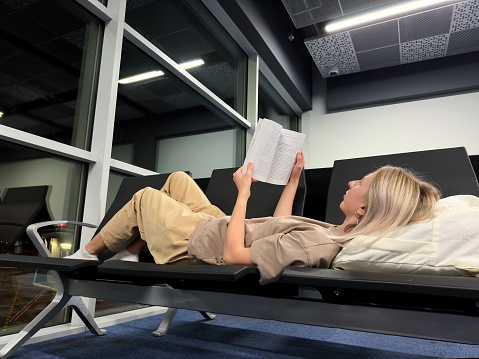 The girl lies in an empty departure hall and reads a book